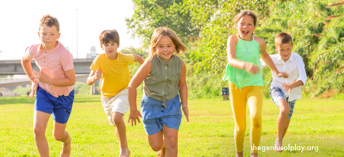  school age kids running happily outdoors in the grass near a city bridge